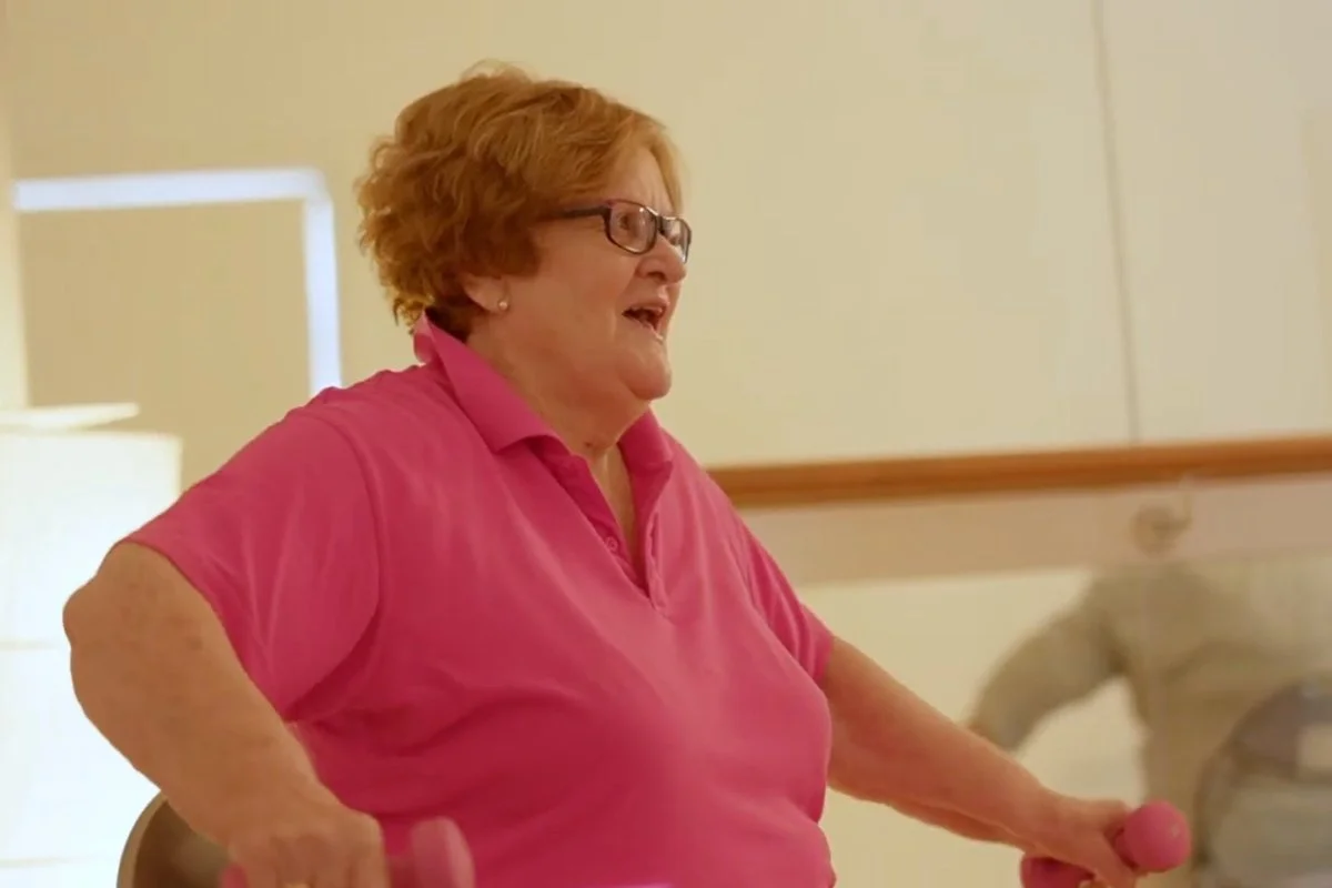 A happy over 60s woman in a pink shirt lifts pink weights.