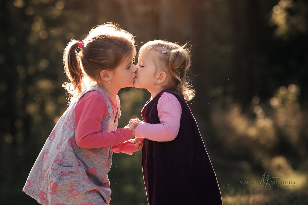  Rodinný portrét dvou sestřiček, které se pusinkují. Fotografie byla pořízená v brněnském parku. 