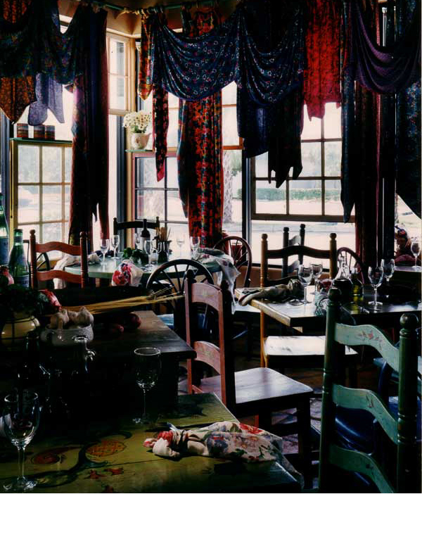  Trattoria seating area is surrounded by market displays, canned goods in windows, and bright cotton printed curtains. 