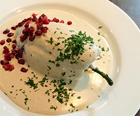  Chile Poblano filled with picadillo (chopped beef and pork meat, nuts, fruits and spices) topped with a Nogada Sauce (walnut-based dairy sauce) garnished with pomegranate seeds and parsley.