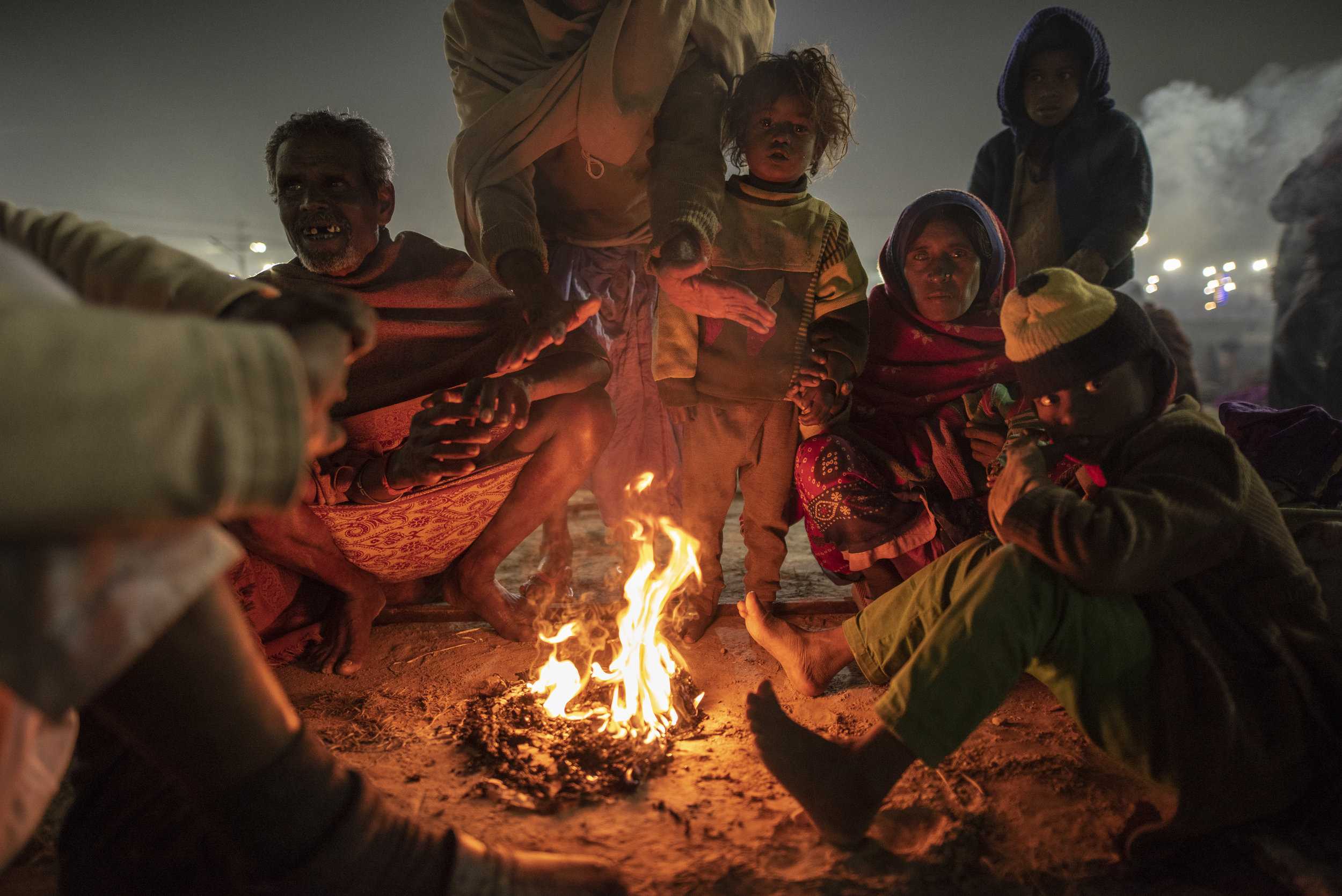  Huddled by a fire, a family gathers on the outskirts of the Mela, preparing for their morning walk to Ganga. 