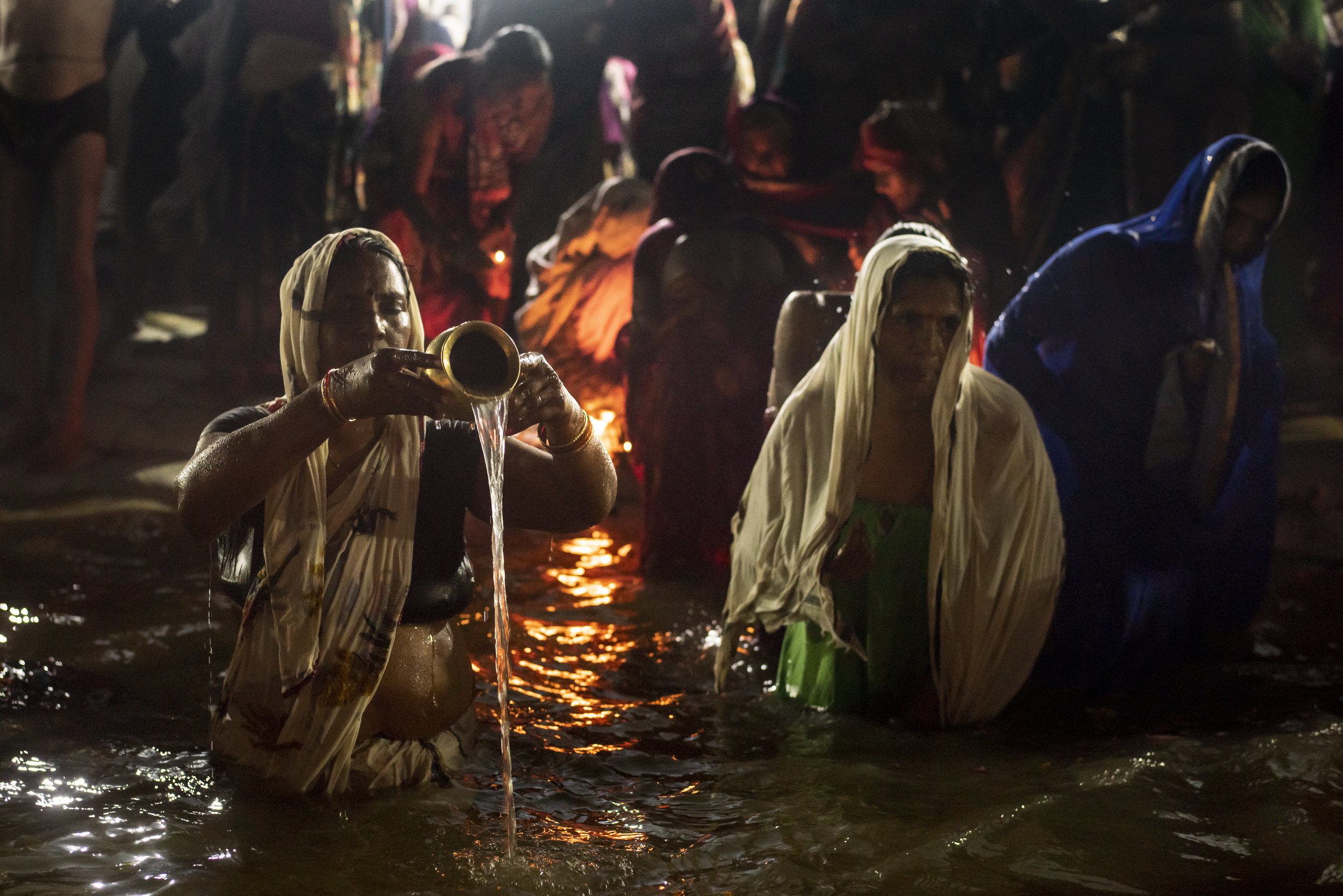  Women gather at the shores of the ganges, pouring water from lota pots, lighting puja offerings and performing ablutions 