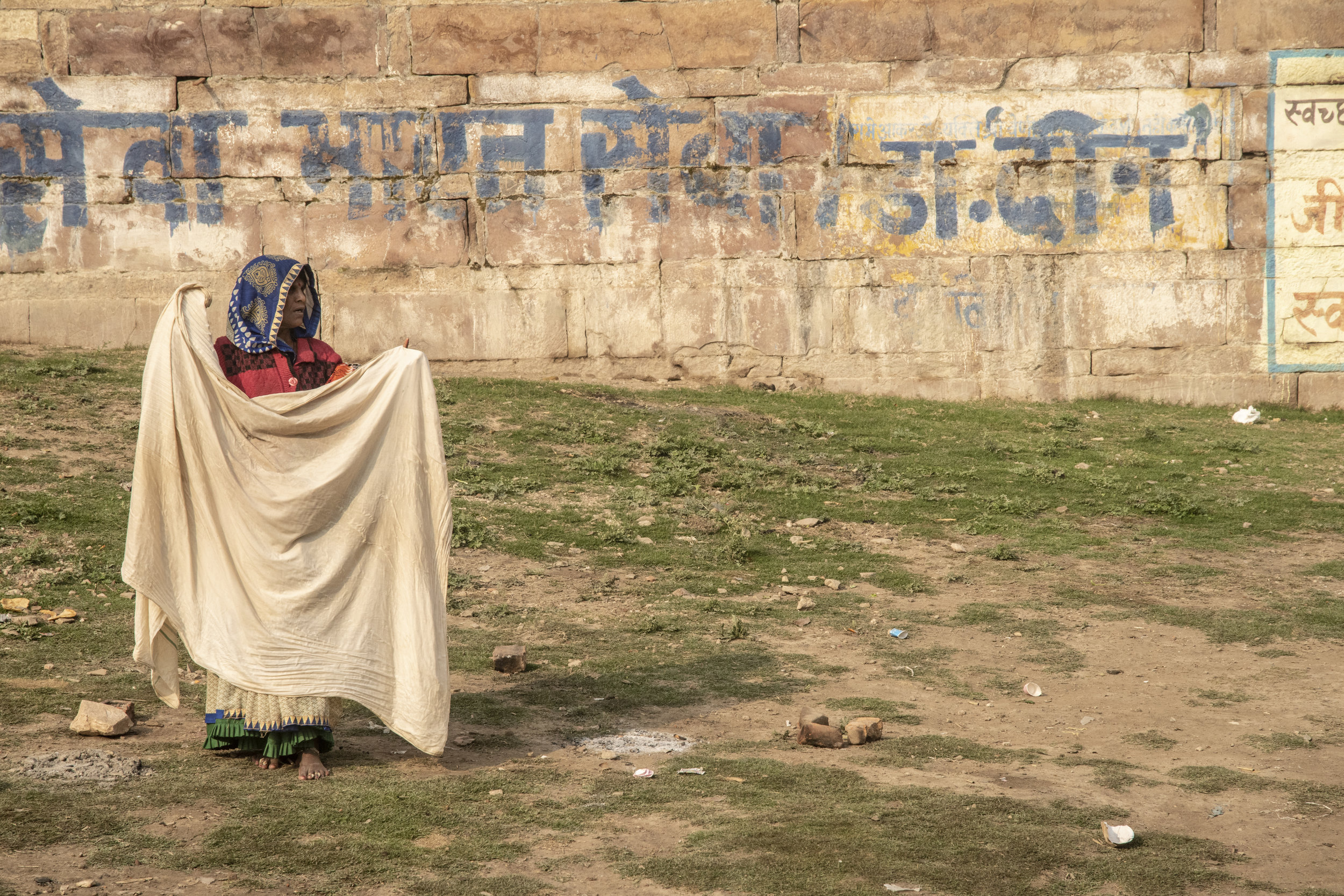 Woman stands afield, drying clothes in the sun