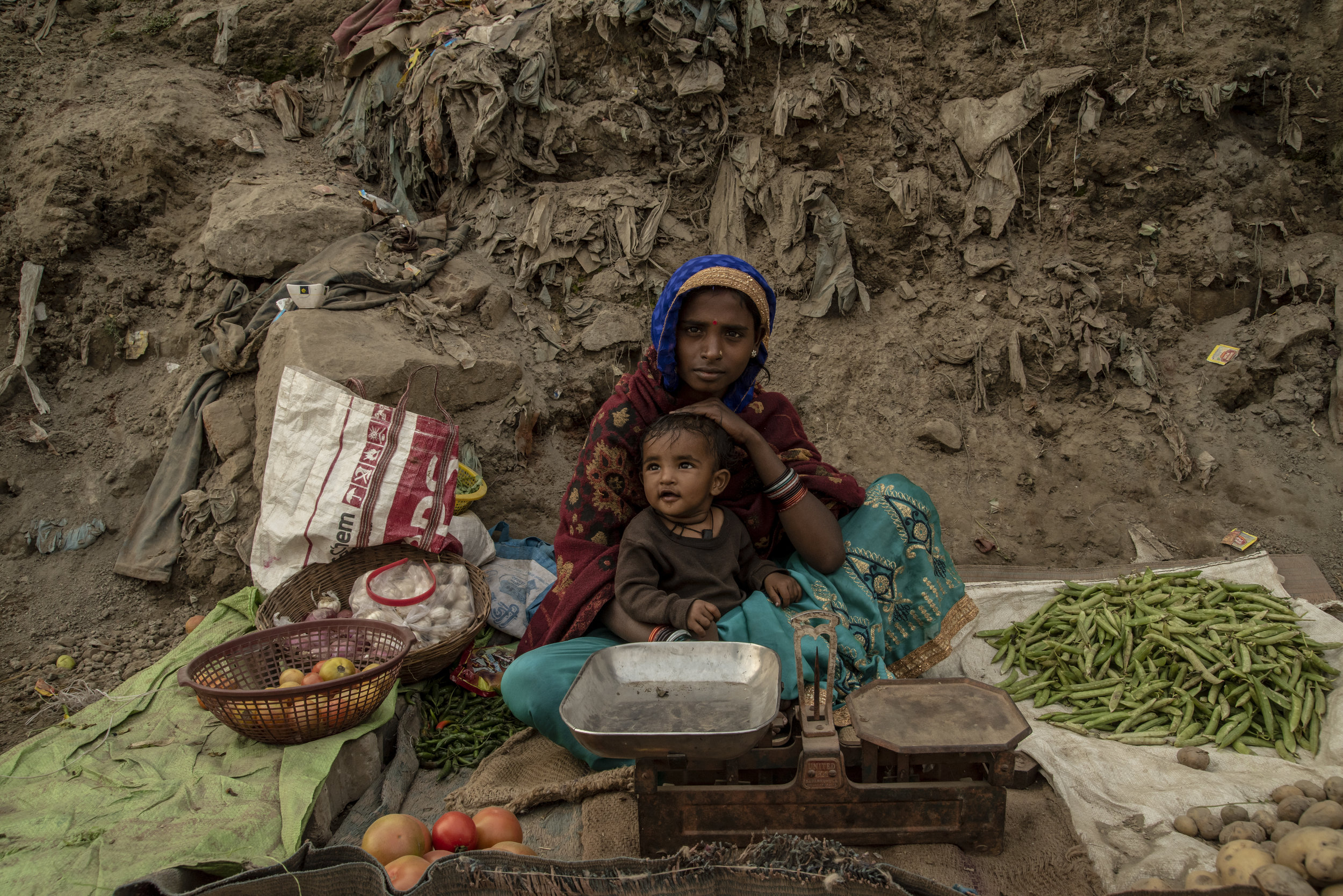 A mother sits with her toddler and sells produce roadside.