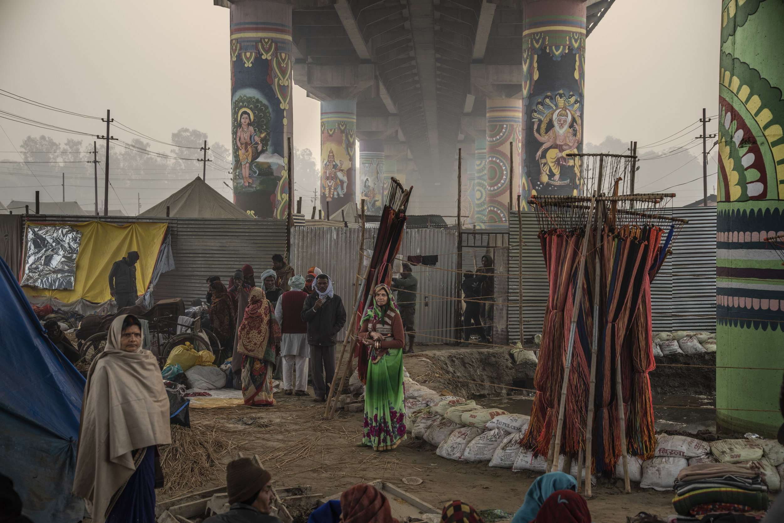 People gather beneath a painted cement bridge within the Mela.