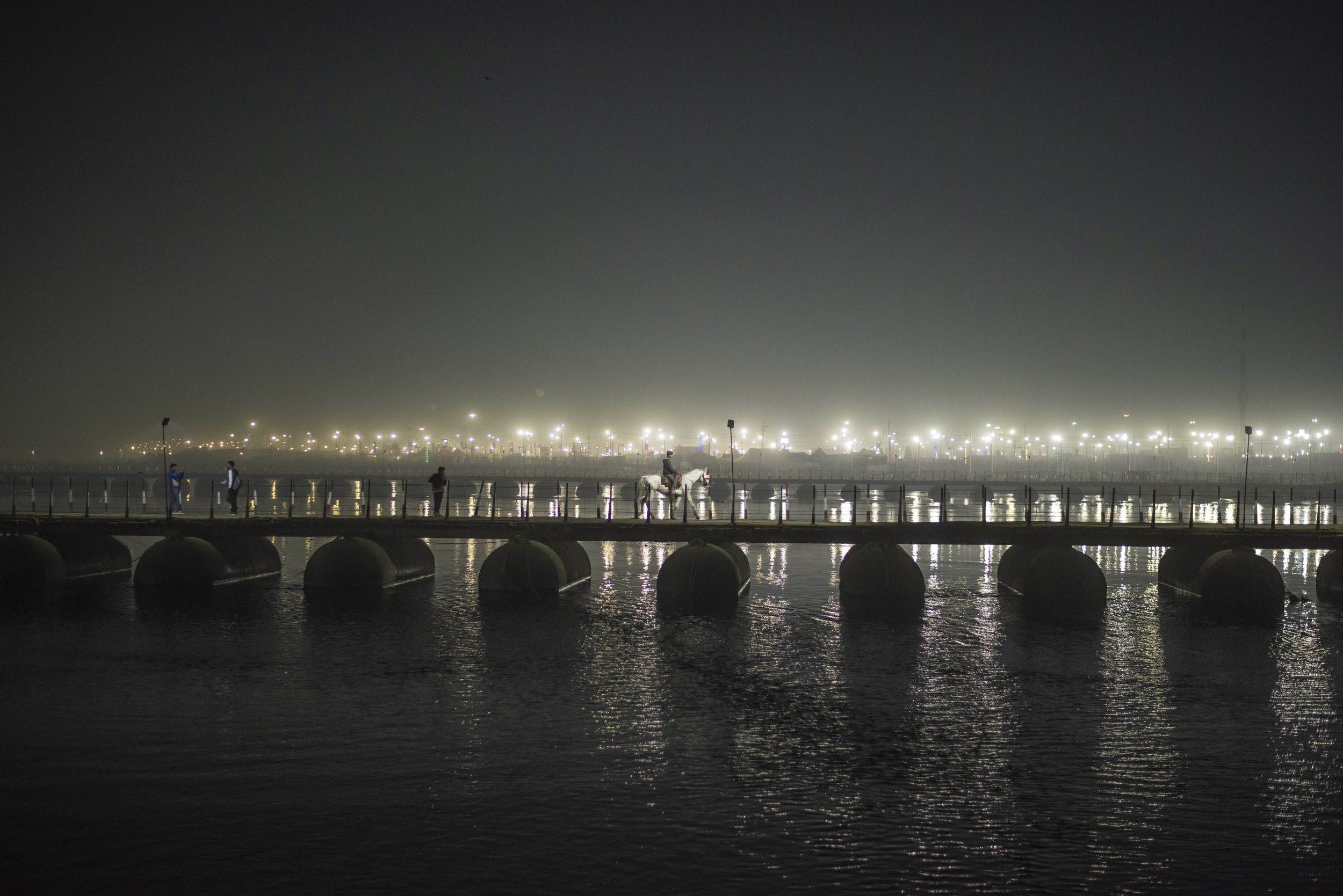 A lone white horse and its rider cross the temporary bridge towards Sangam
