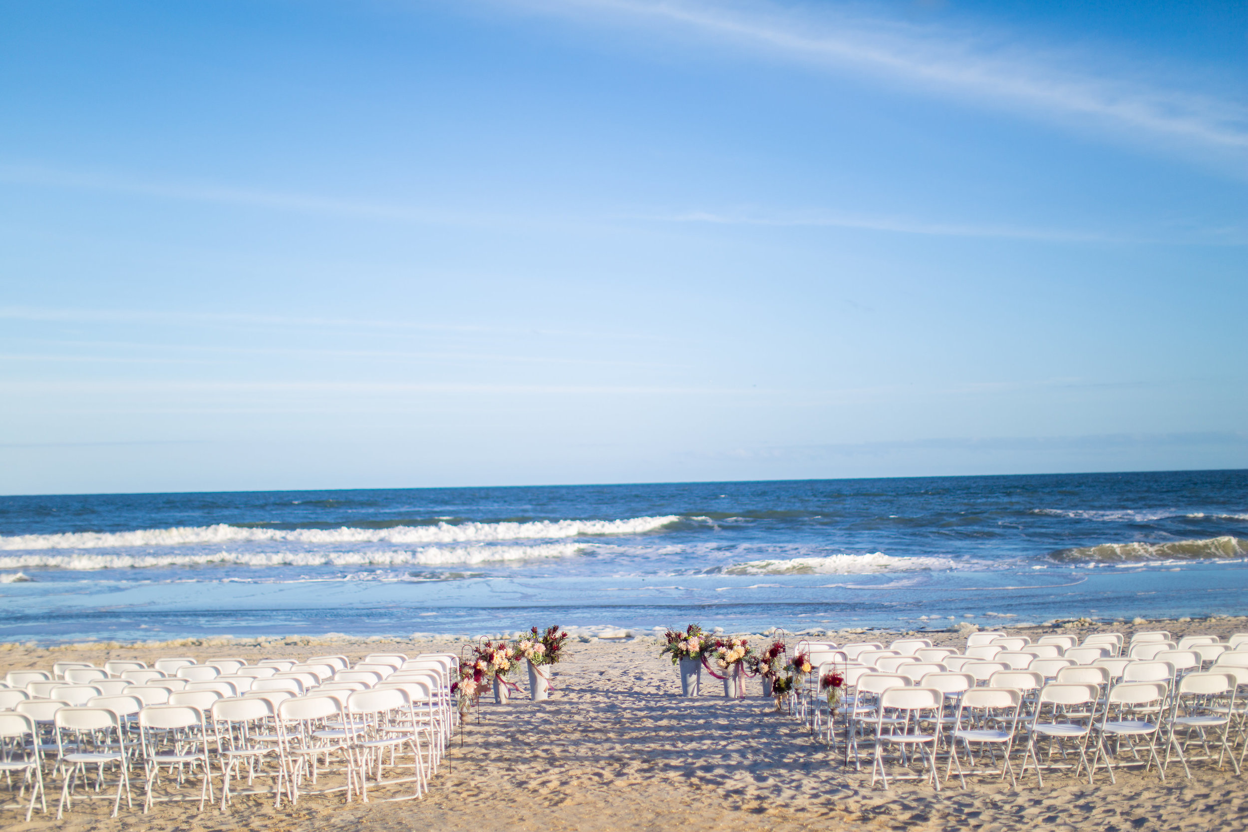 We loved the simplicity of Jenna and Jon's ceremony space. The white folding chairs leave little to distract from the crashing waves of the ocean and blue skies. The pop of color in the aisle arrangements and galvanized buckets at the altar brought all the focus to the couple as they said their vows. 