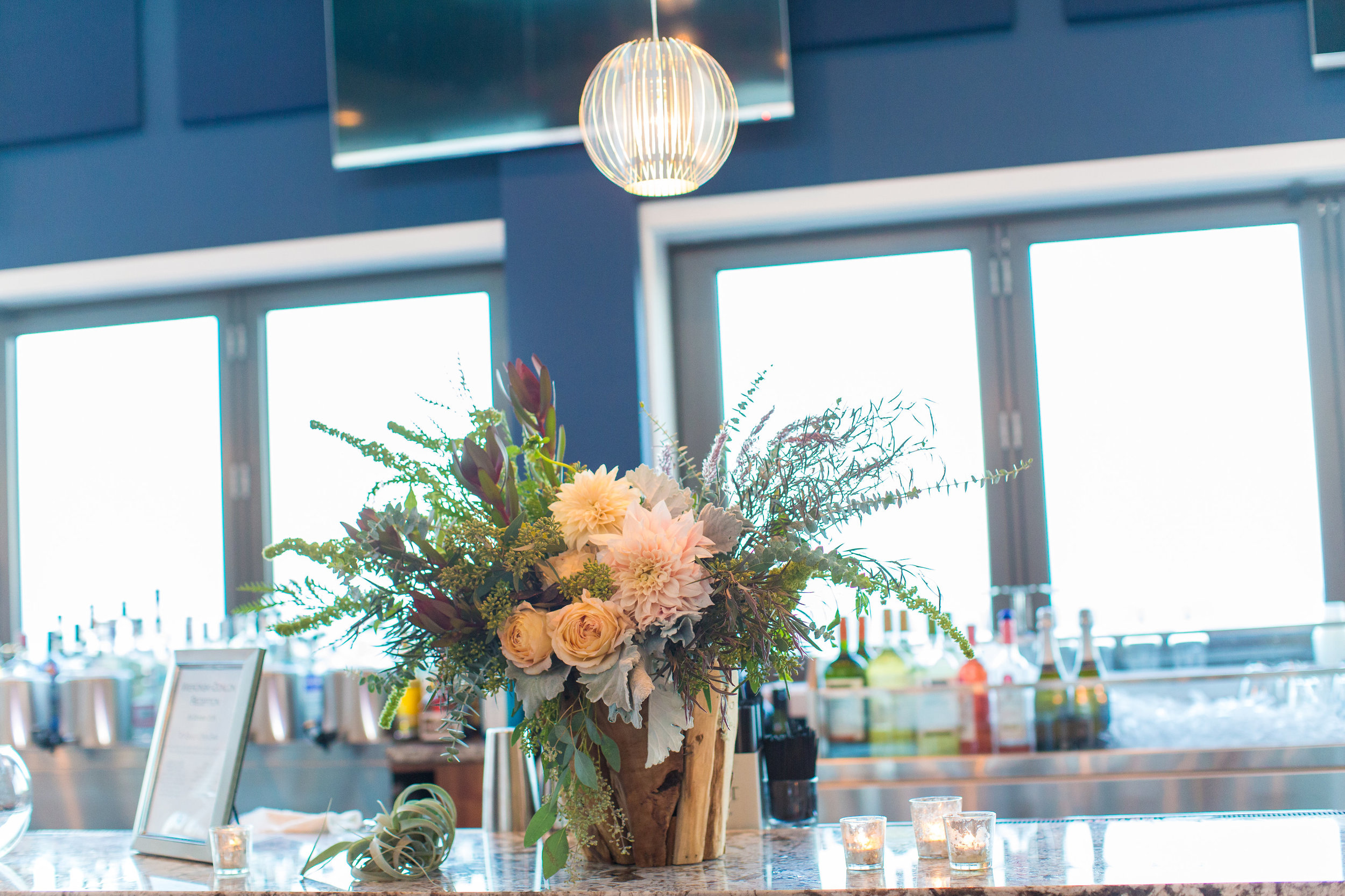 A beach wedding never feels complete without our driftwood vase making an appearance - and it always looks so different! This wild look of dusty miller, roses, dahlias and a forest worth of greenery made this arrangement a great statement piece for the bar. 