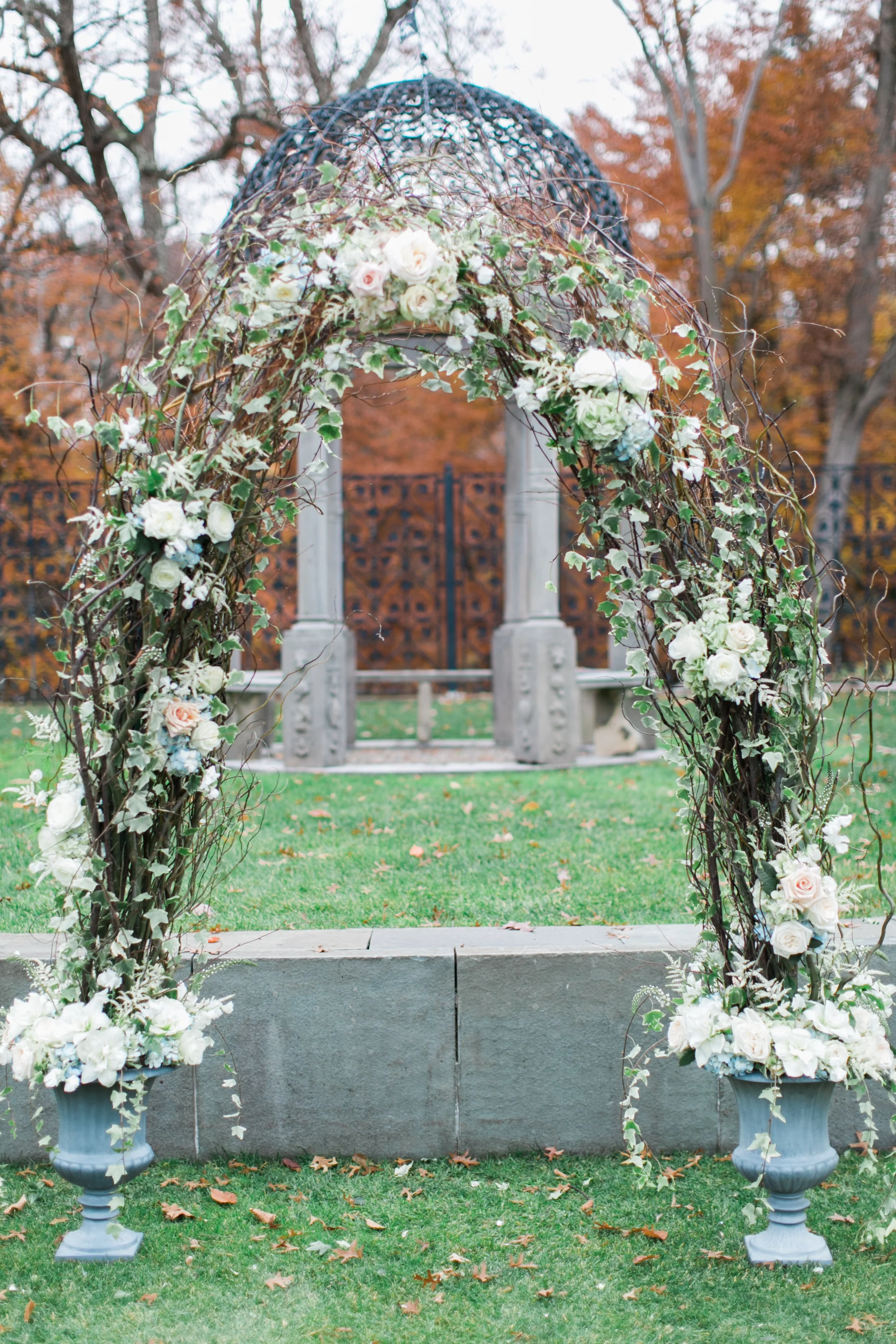 We used our large grey urns for the ceremony decor, connecting them with branches, and loose flowers to create an arch for the couple to stand under. Roses, hydrangea and ivy helped soften the look of the curly willow. 