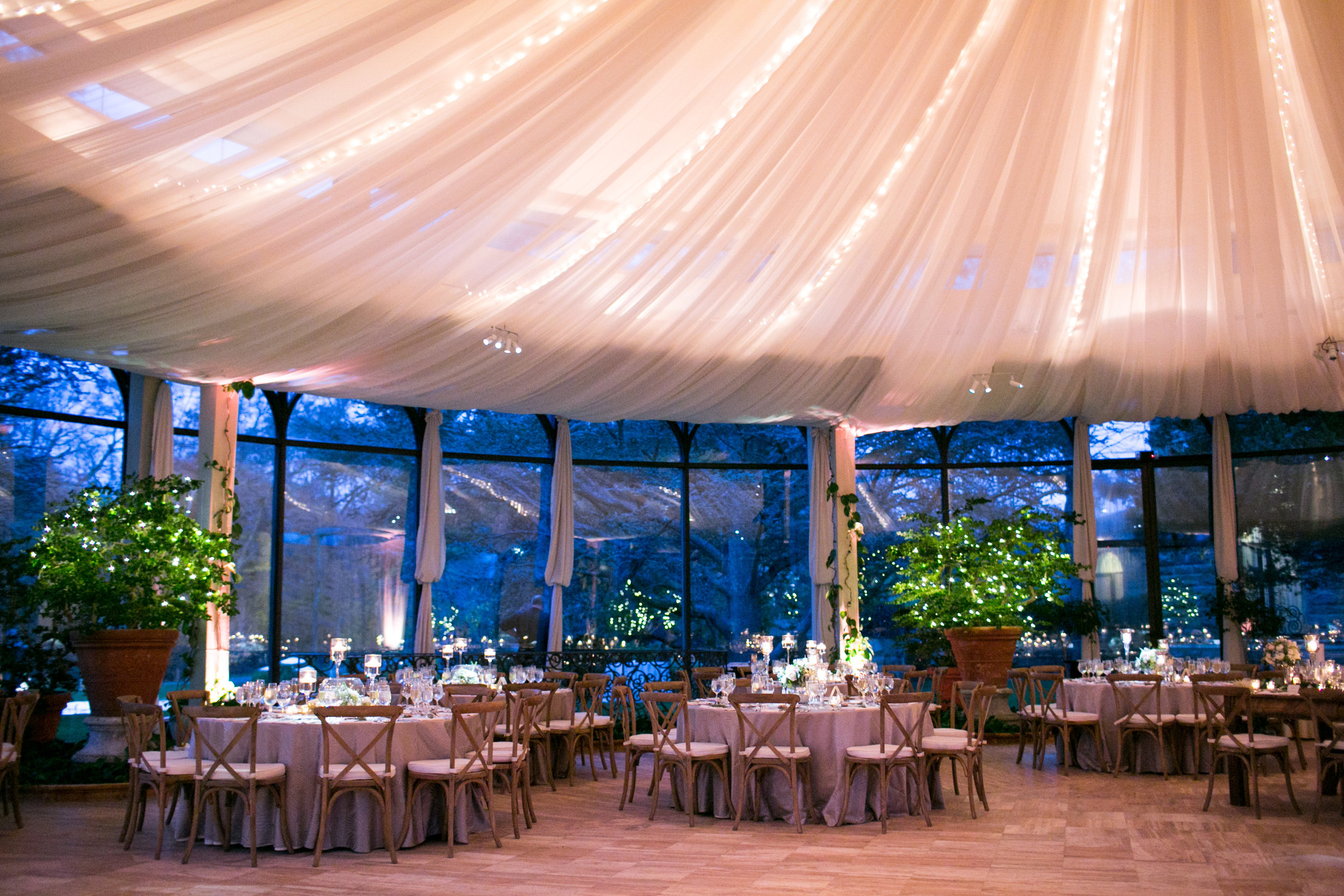 This reception room is to die for! Sarah and Steven added draping to the ceiling for an extra dramatic flair, with string lights bringing even more ambiance to a room filled with candleight. Jasna already provided the giant planters with trees dazzled with more string lights to brighten up the room and break up the window space. 
