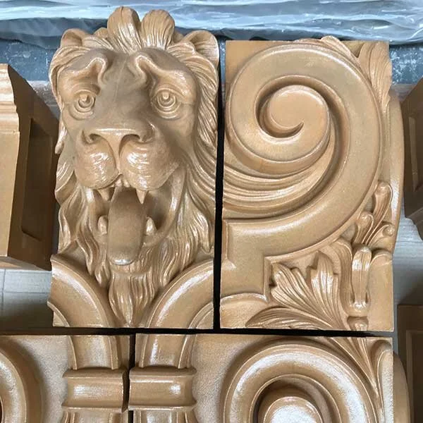 Decorative carving featuring a lion's head with an open mouth and a flowing mane, alongside ornate swirling patterns and foliage designs.