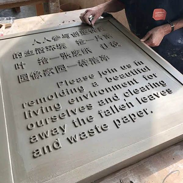 A person carving a sign with both Chinese and English text on a wooden board.