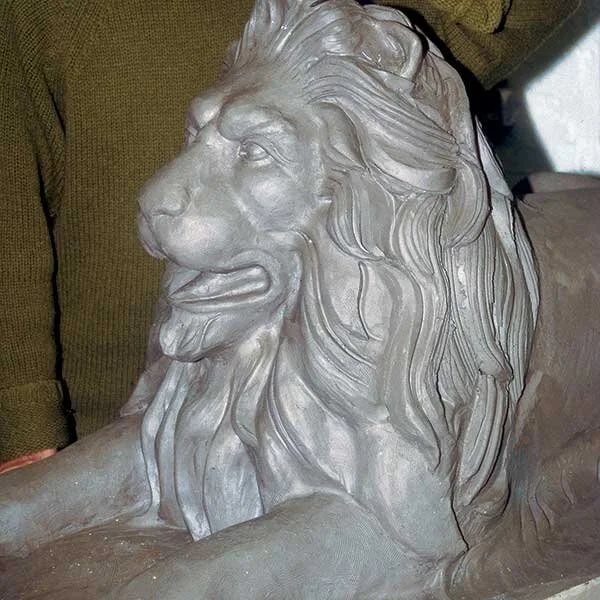 A detailed sculpture of a lion's head, showing a mane and facial features, resting on a piece of furniture.