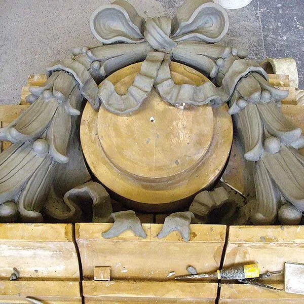 Close-up of a carved stone decorative element, possibly part of a larger sculpture or architectural detail, with a circular wooden base and wooden blocks around it.