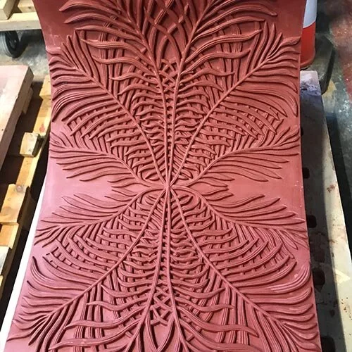 A carved wooden panel featuring an intricate symmetrical leaf pattern with detailed veins and edges.