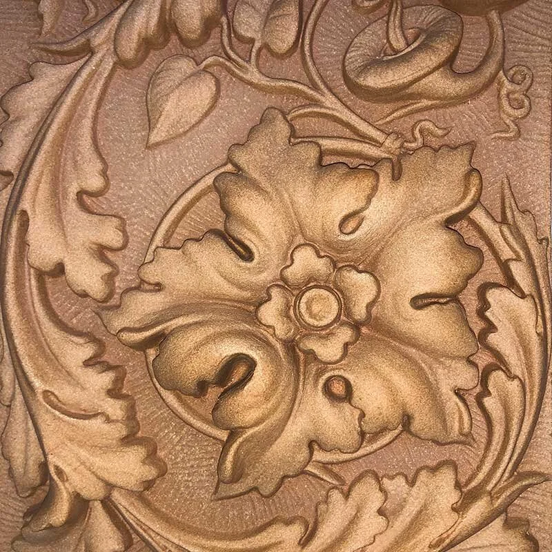 Close-up of an ornate carved floral pattern in wood or metal with detailed swirling leaves and a central flower motif.