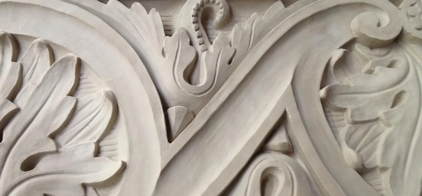 Close-up of an ornate carved stone or plaster architectural decoration with intricate floral and scroll patterns and a small serpent design.