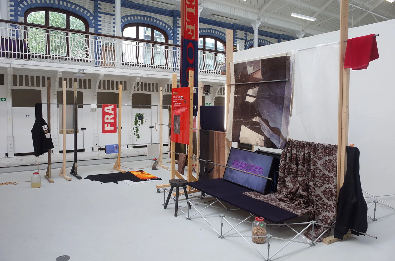 KOBBY ADI A GENTLER FLAME, 2018 A true and exact materials list: joy, reactive digital prints on linen, reactive digital prints on heavyweight canvas, wood, wooden beads, steel, mummy, stools, matchboxes, statues, hotel bathroom sign, jar containing palm wine, jar containing water from the Atlantic Ocean, jar containing loose wooden beads, jar containing infected plant and chicken bones, various fabrics, Commonwealth Institute cinema programme, Commonwealth Institute pamphlet, books, plant, hd video, bubble wrap, felt hoodies, ex military patches, quilt, wool, lightbox, UV print on found acrylic, UV print on dibond, wool knit, Dimensions variable Courtesy the artist, Photo: ARK