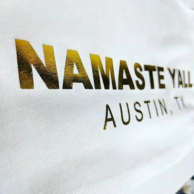 Specialty gold foil screen printing on white yoga apparel tees reading Namaste Y'all in Austin, TX.