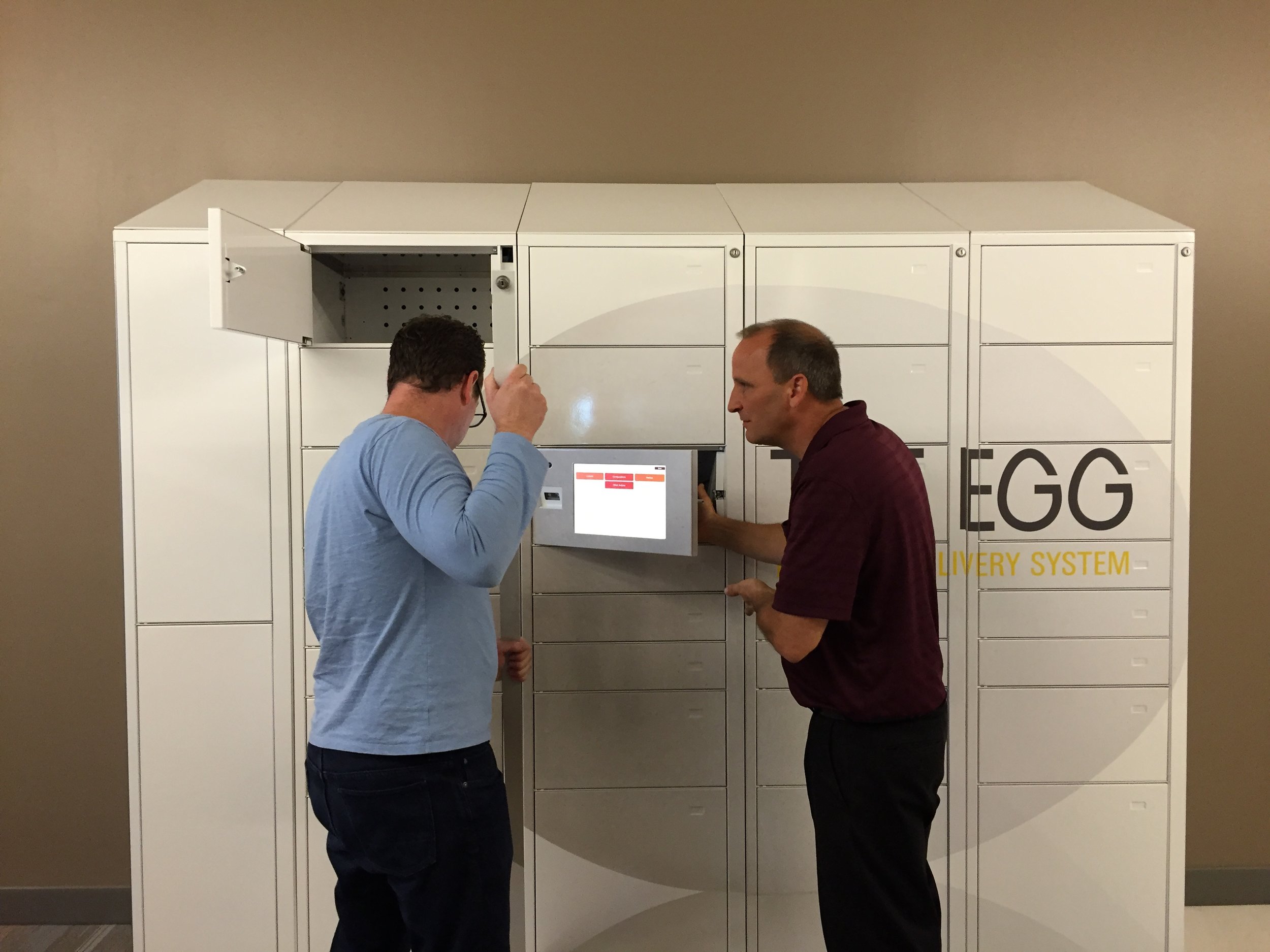Two men examining the Egg lockers and old interface and tablet