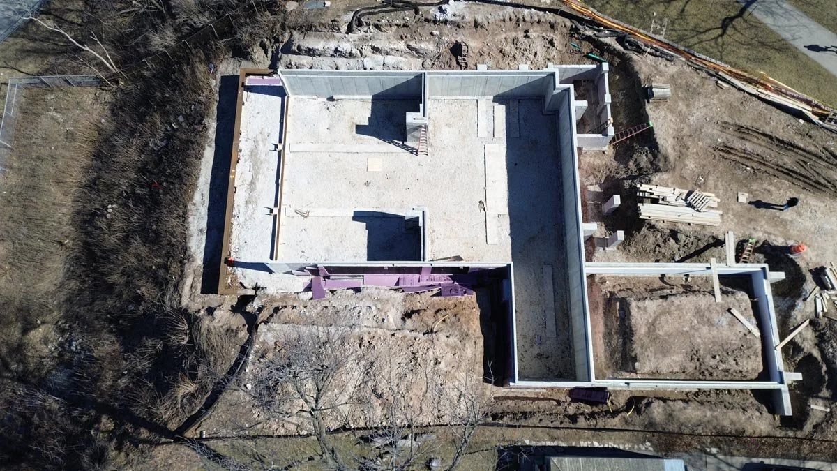  Aerial view of poured concrete foundation walls and basement slab at an excavated construction site. 