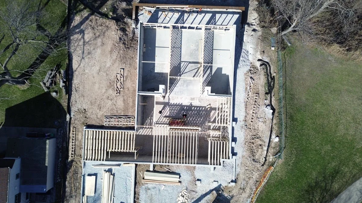   Overhead aerial view of floor trusses being installed over a concrete foundation, with lumber staged on a gravel site. 