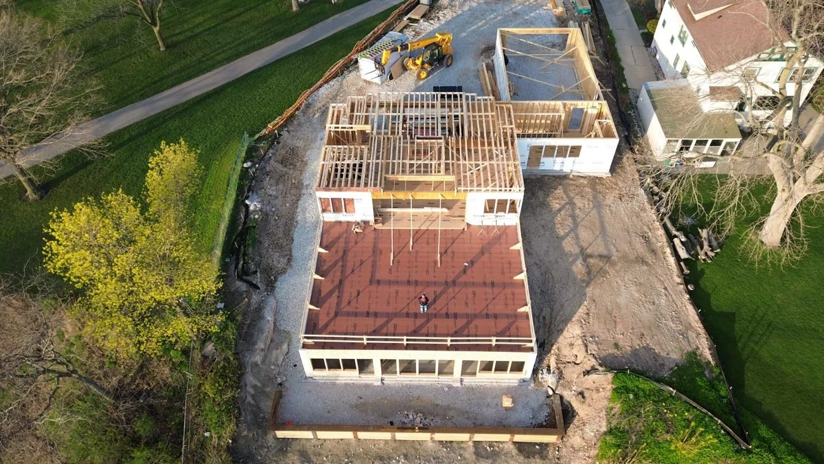  Aerial view at dusk of second-floor wall framing going up on the house, with the garage framed alongside. 