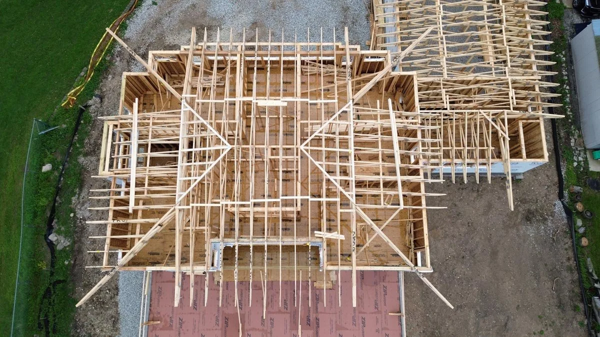   Overhead aerial view of hip roof trusses set on the main house and garage, above wrapped walls and a red-sheathed terrace deck. 