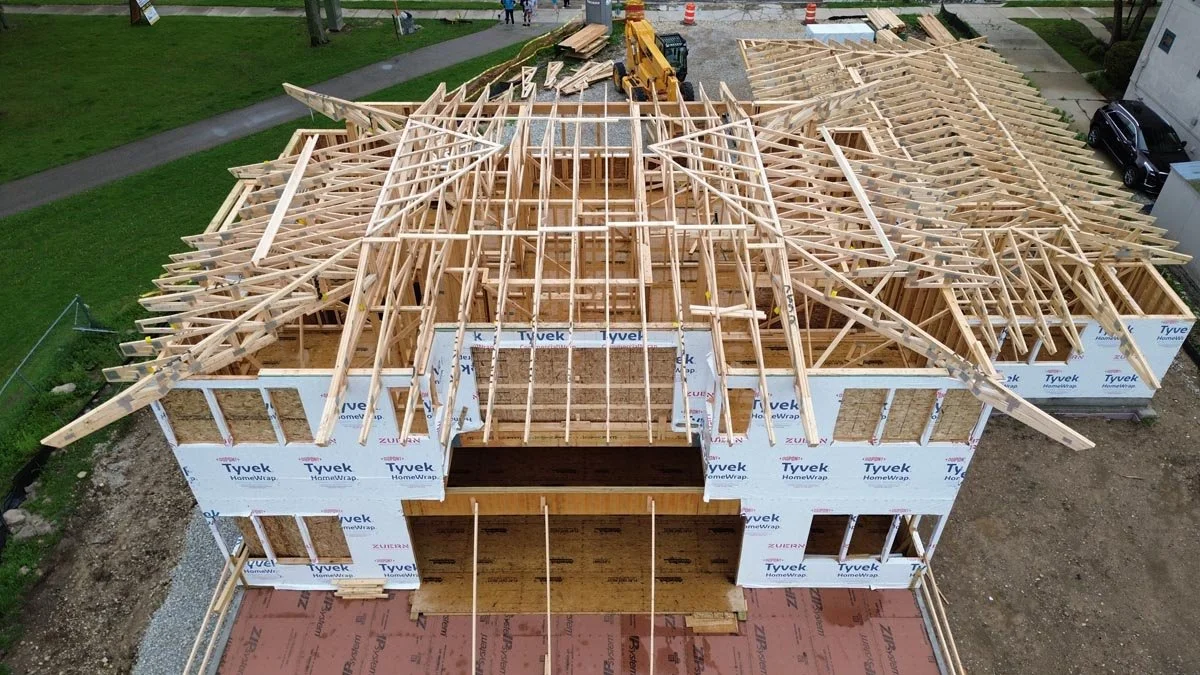  Aerial view of roof trusses being set on the two-story house, with walls covered in Tyvek house wrap. 