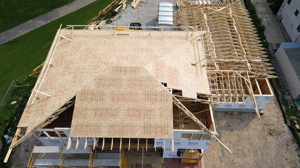  Aerial view of the main hip roof partly sheathed in plywood, with the garage roof trusses still exposed. 