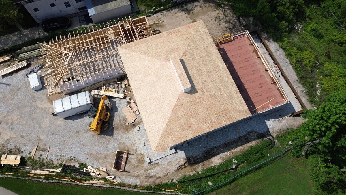  Top-down aerial view of the fully sheathed hip roof with the chimney framed, beside the terrace deck and garage framing. 