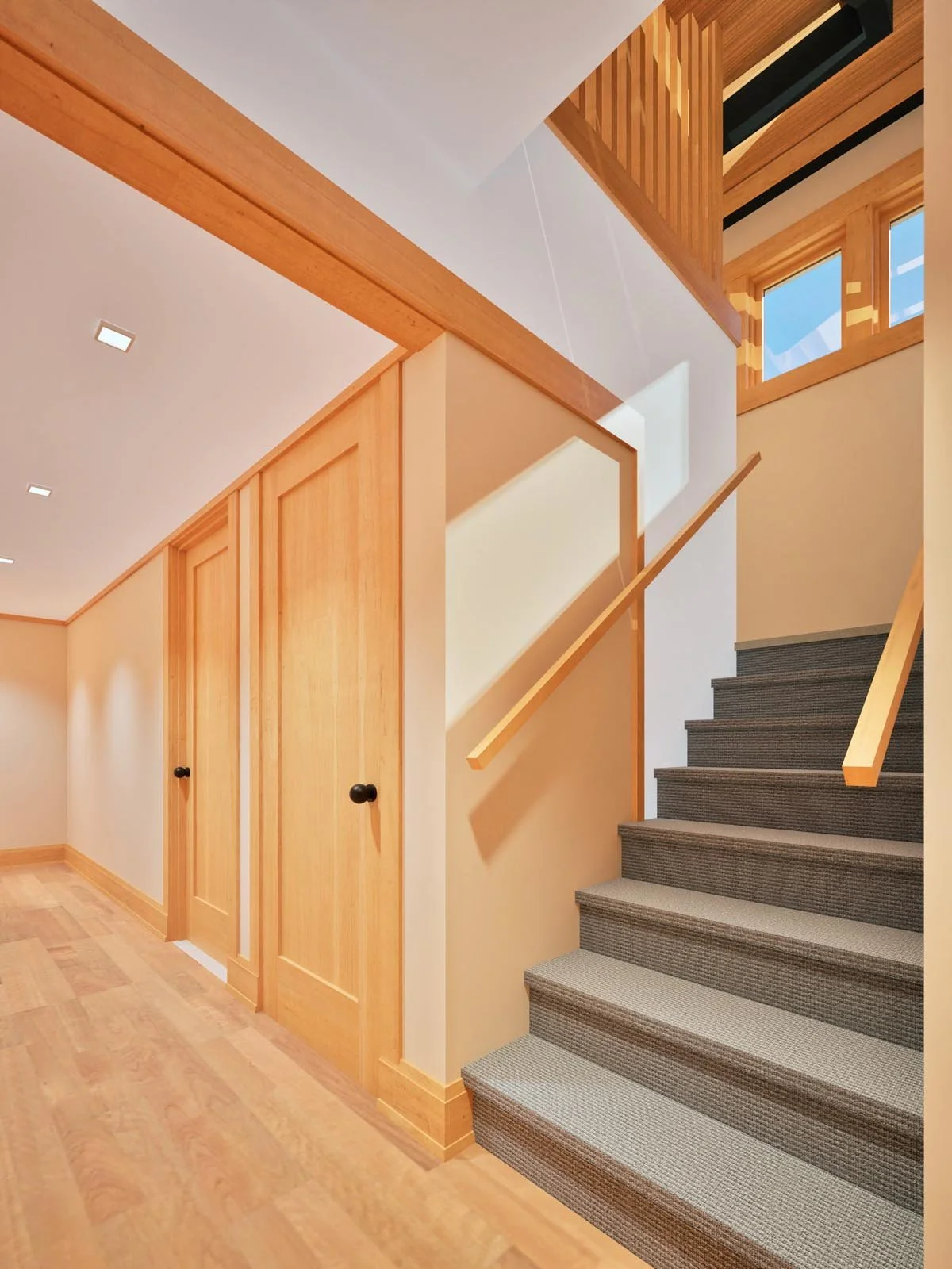  Rendering of a basement hallway with light wood floors, paneled wood doors and a carpeted staircase leading up toward clerestory windows. 