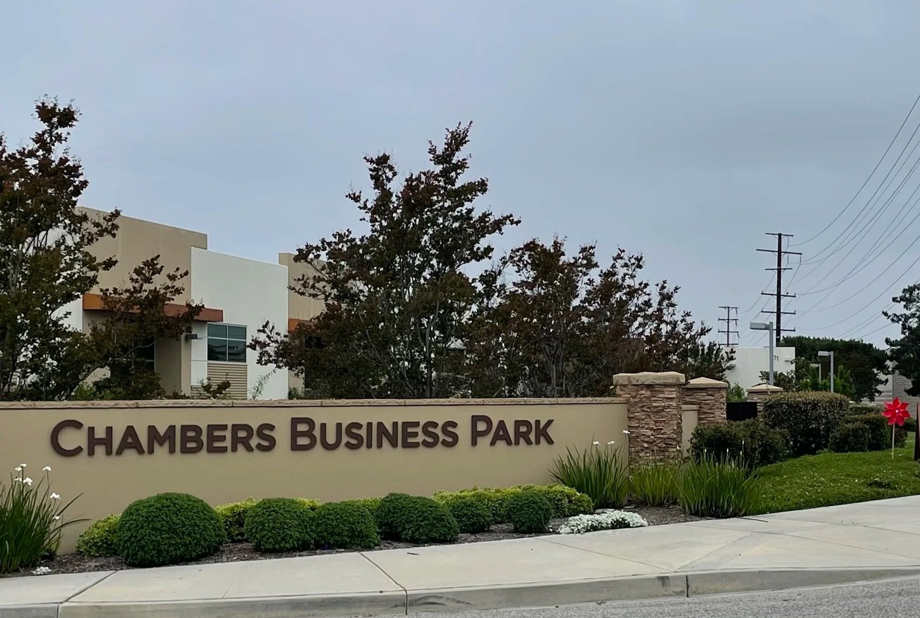 Entrance sign for Chambers Business Park with landscaping, bushes, and flowers, and part of buildings and power lines in the background.