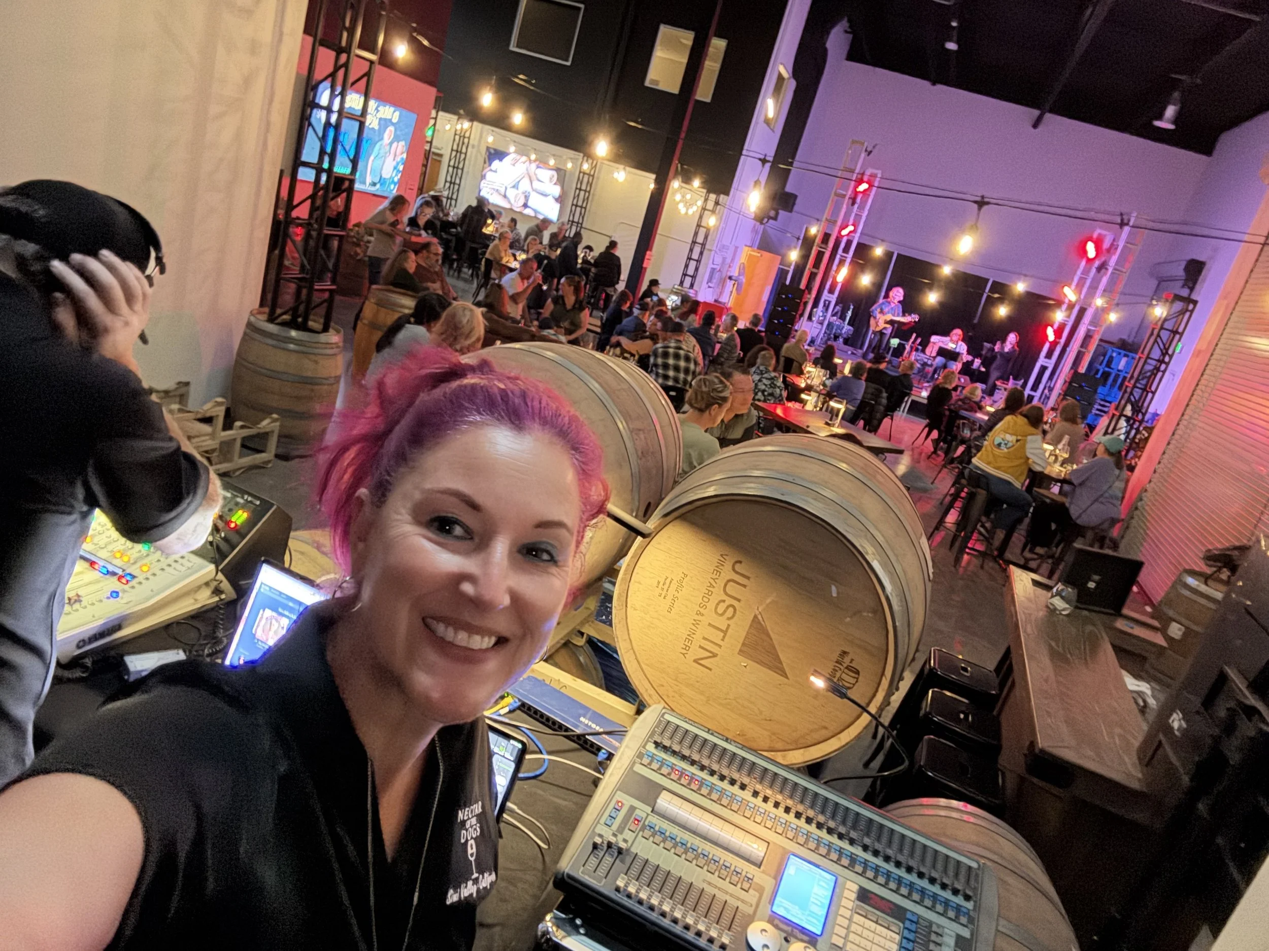Woman with pink hair showing the packed room with a live band on stage and audio engineer working the board.
