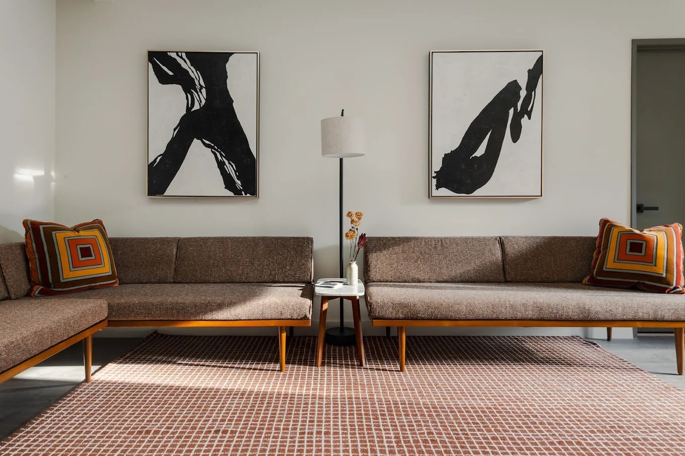 Waitingroom in Los Feliz therapy office. Large abstract black and white paintings above warm-toned midcentury sofas, lamp, and clean, graphic print rug.