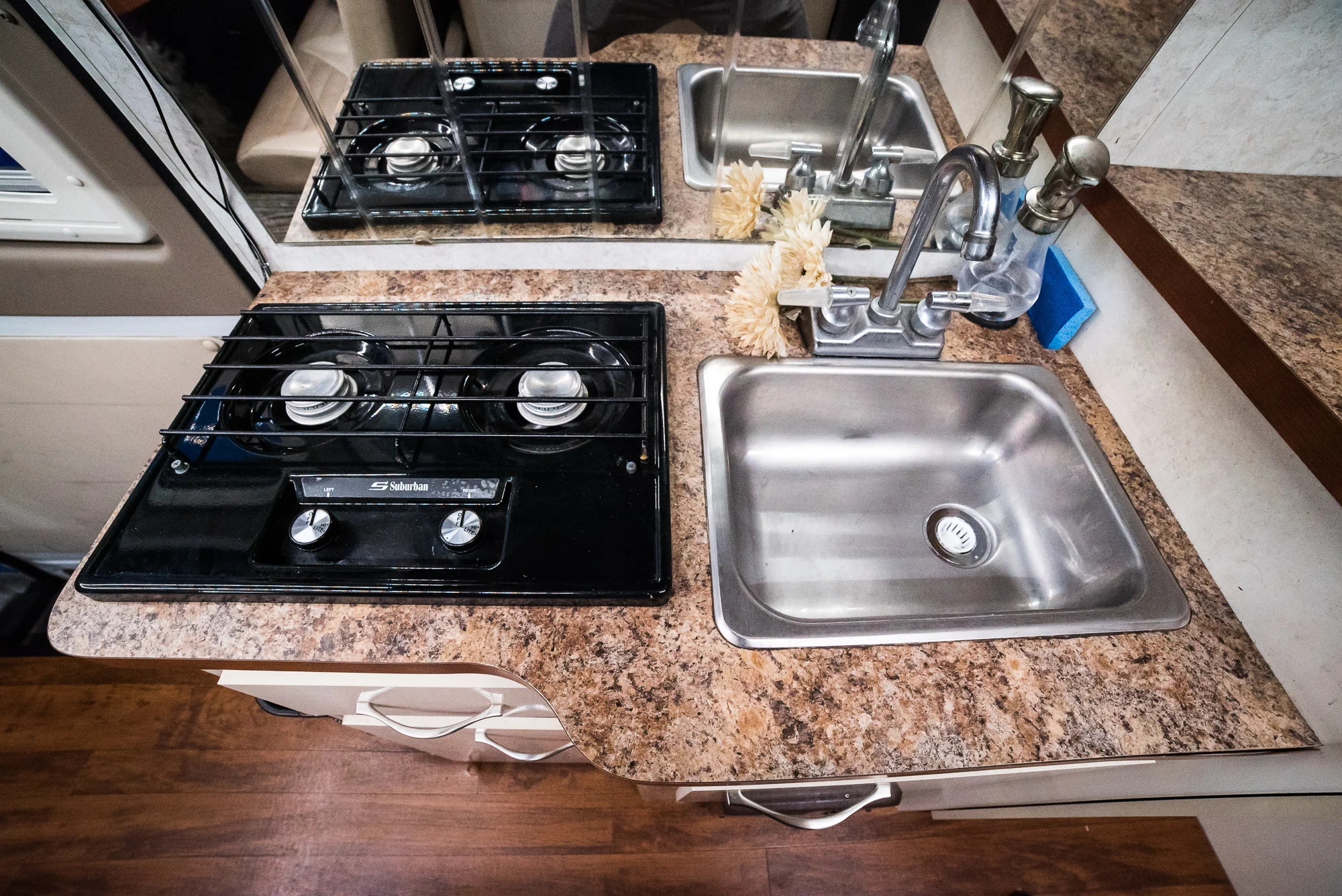 See? Kitchen. That's a two-burner propane stove on the left. The sink is fed by a 24 gallon fresh water tank and it goes into a 12 gallon gray water tank, which I have to empty about once a month. Silverware drawer is on the left with an "everything" cupboard beneath it, containing mostly tools and cleaning supplies. The cupboard on the bottom right is my pantry with all my dry and canned goods. Counter space for chopping just to the right.