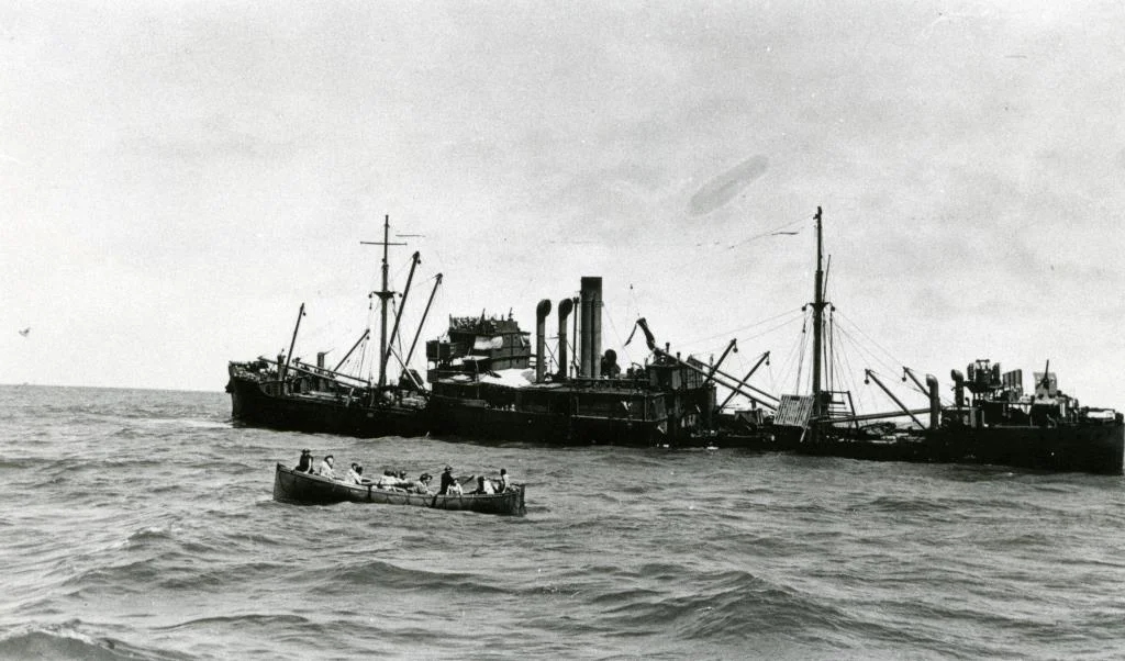 The merchant ship, Macumba, after it was hit. Many survivors were saved via life boats (foreground).