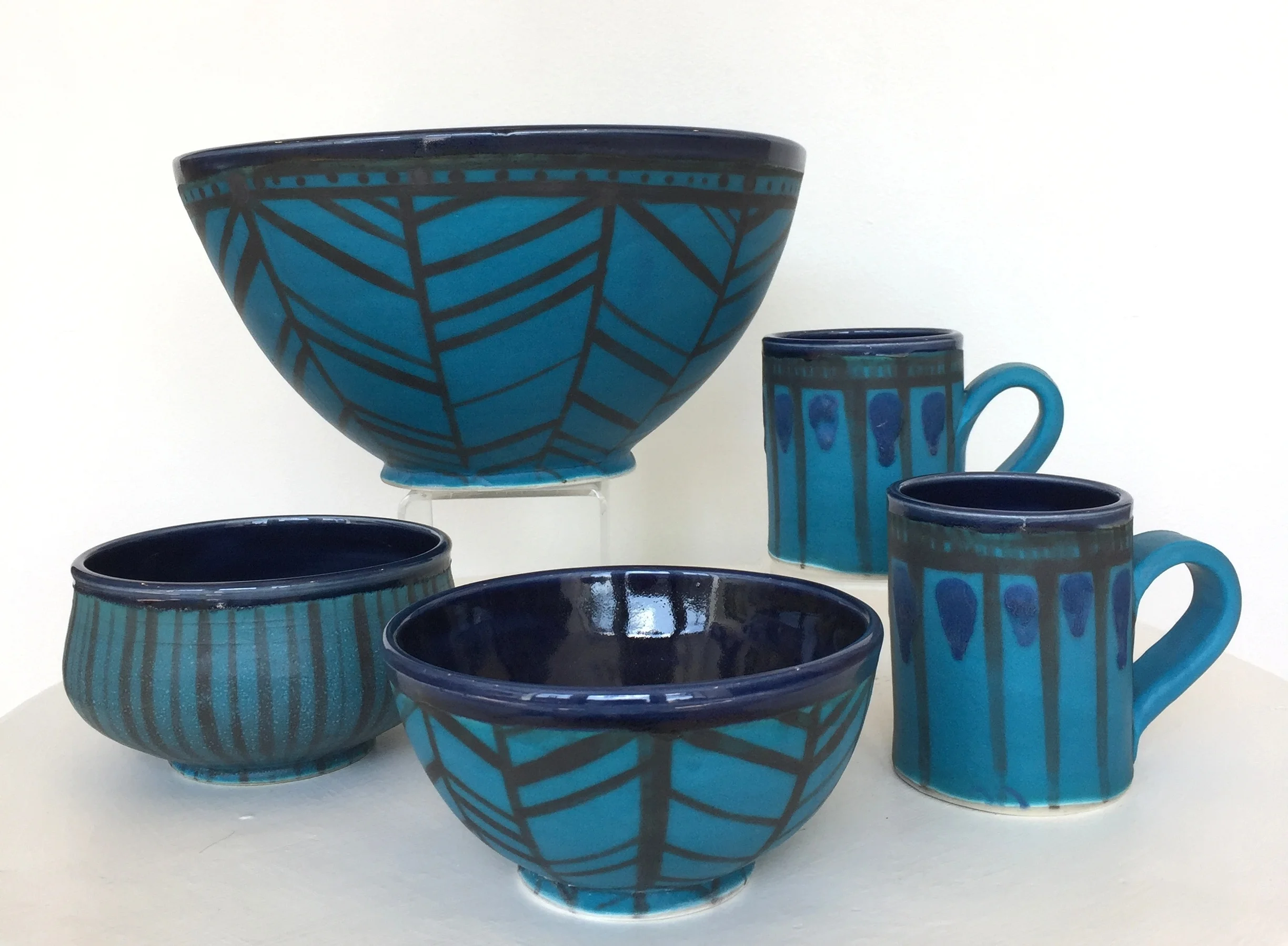 Ceramic bowls and mugs with turquoise exterior and navy interior, herringbone, stripe, and abstract patterns, $38-$150