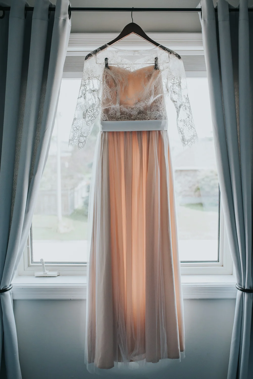 Blush wedding dress with off white lace overlay hanging in the window