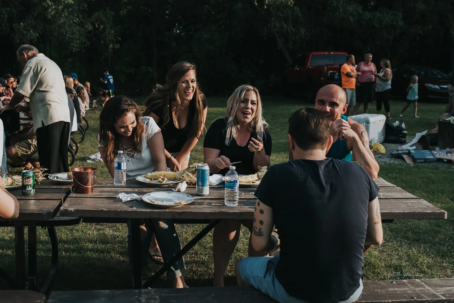 Five friends sitting at a picnic table eating BBQ and sharing a laugh