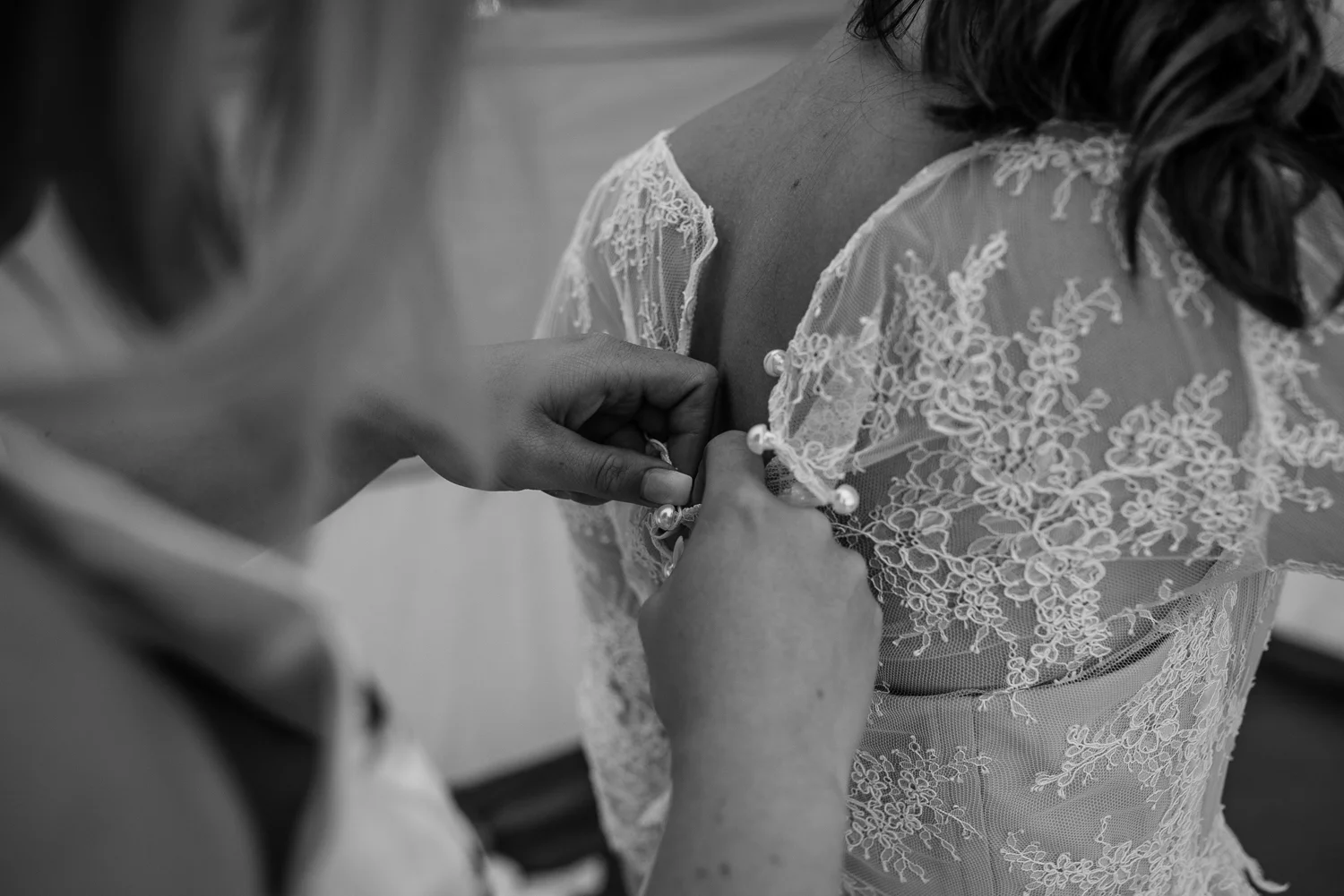 Bride getting into her wedding dress while bridesmaid helps fasten her back buttons