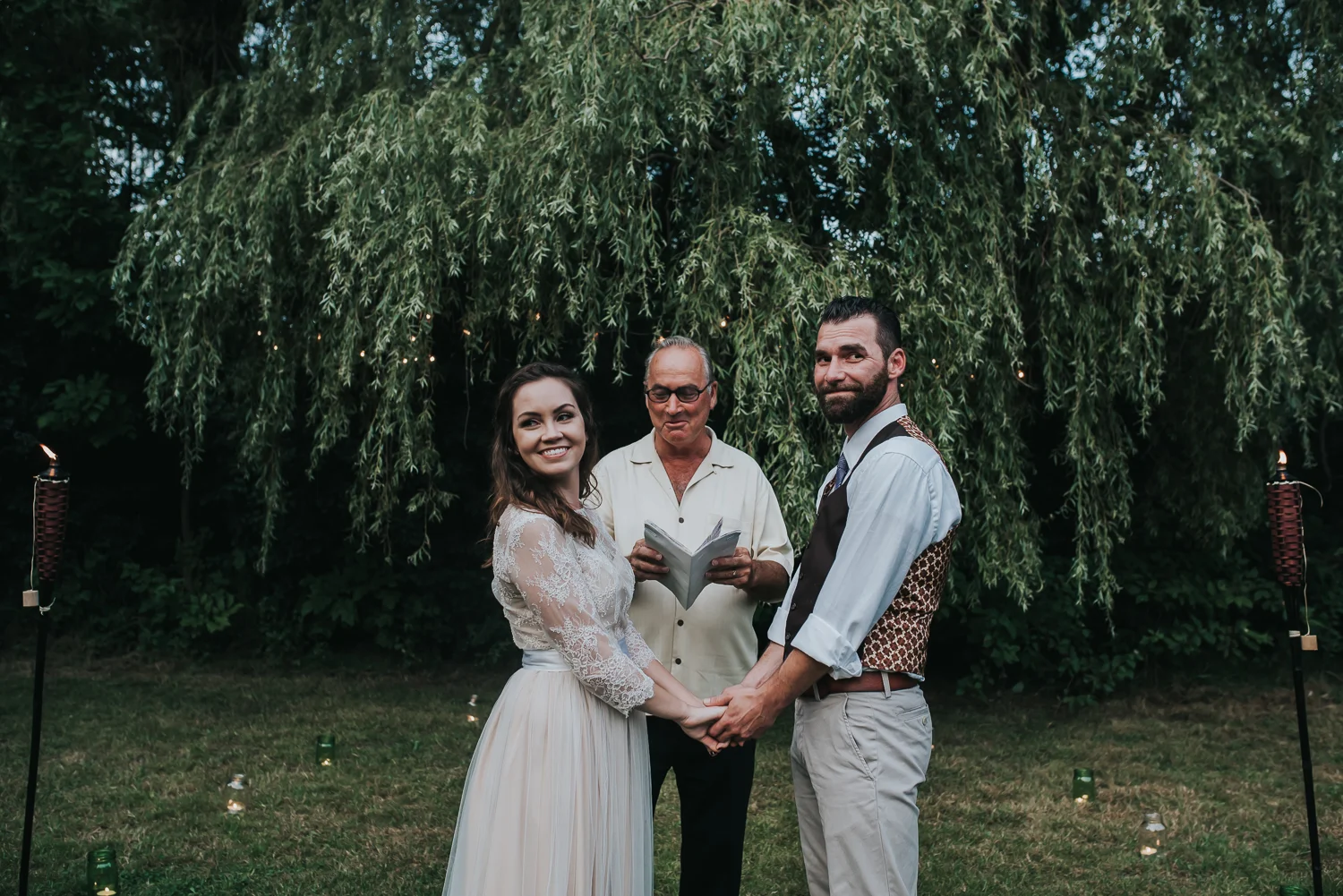 Happy bride and groom in front of their minister looking back at their family and friends with a smile