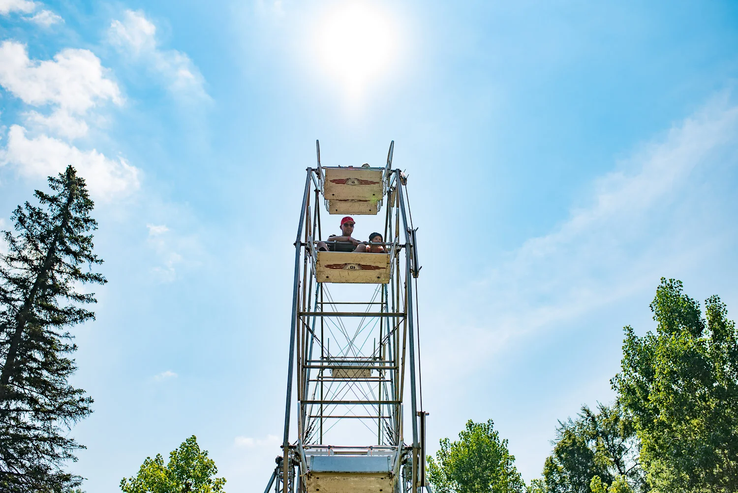 Toddler girl and her dad on a ferris wheel ride at London's Storybook Gardens surrounded by blue sky and green trees