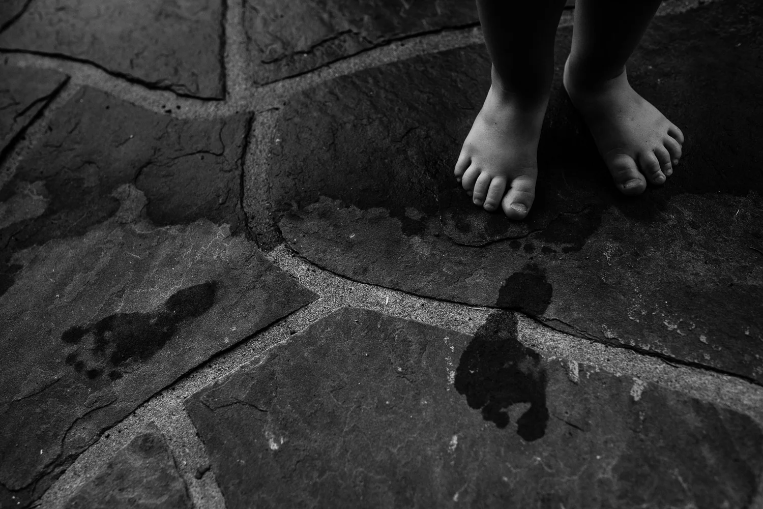 Black and white photo of tiny toddler feet on stone and wet foot prints.