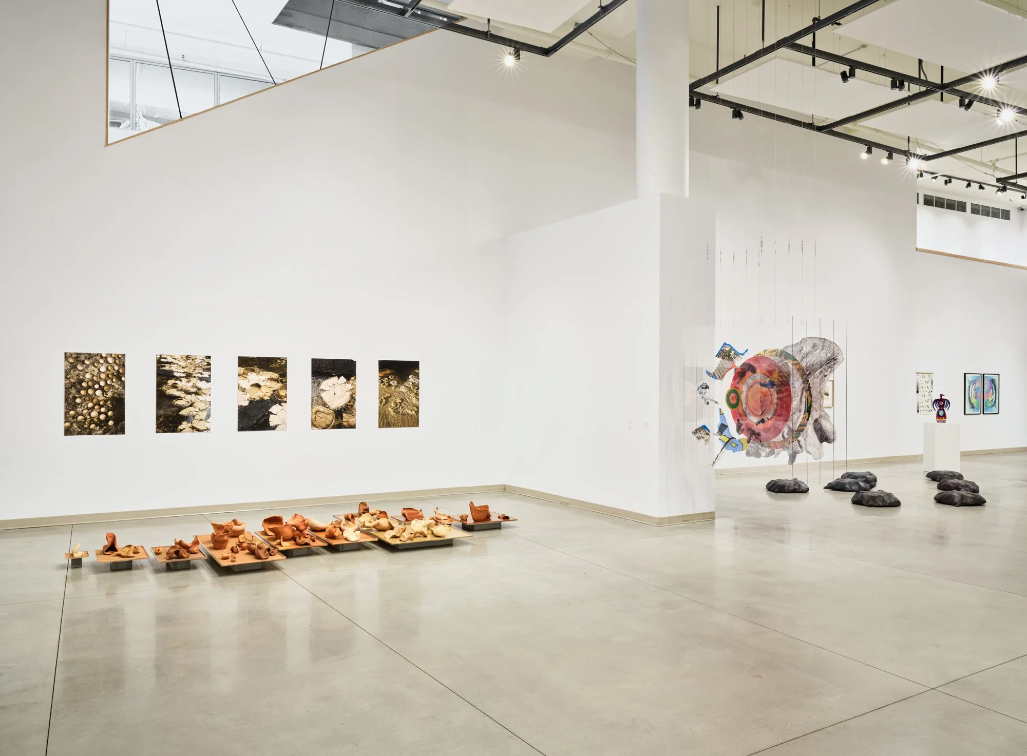 Indoor art gallery with photographs, sculptures, and paintings displayed on white walls and floors.