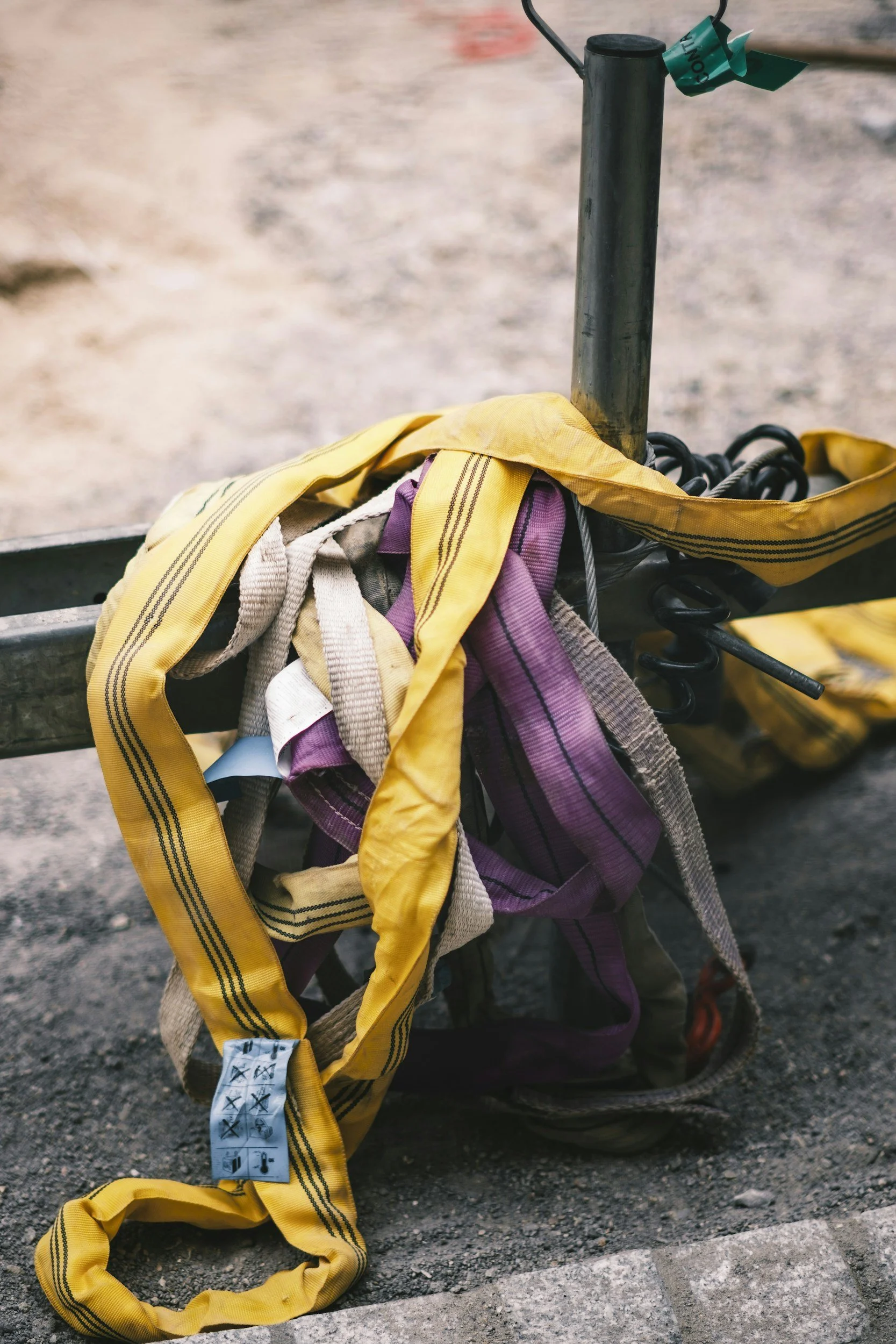 Close-up of a bicycle handlebar with tangled yellow and purple straps hanging from it, set against a gravel road background.