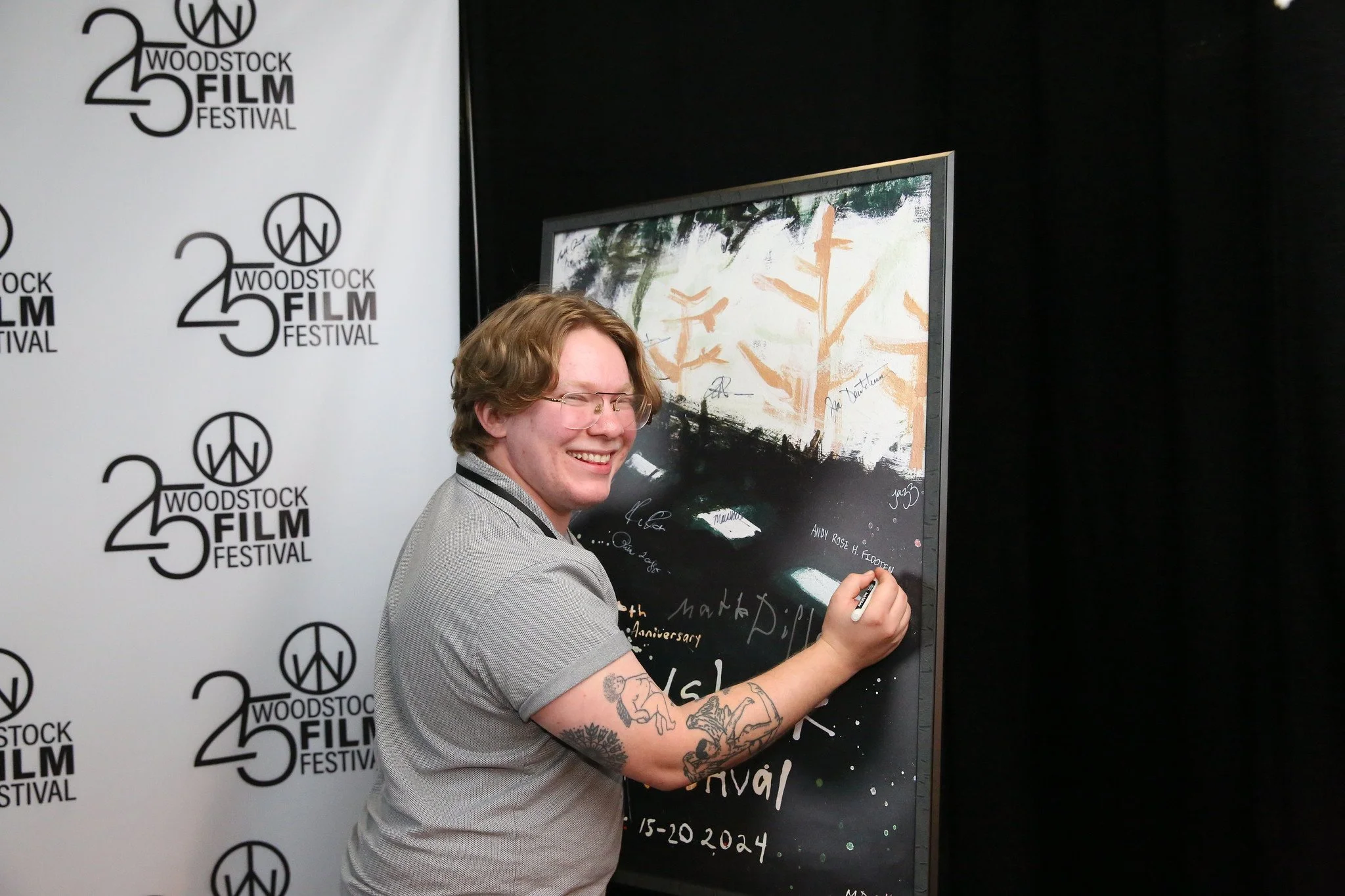 A person signing a blackboard at the Woodstock Film Festival, with a backdrop displaying the festival's logo.