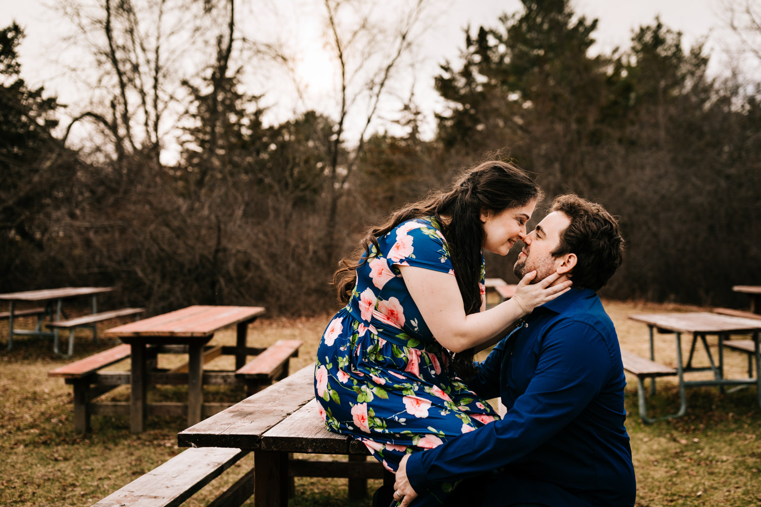 Woman sitting on picnic table kissing man wearing blue floral dress in Massachusetts