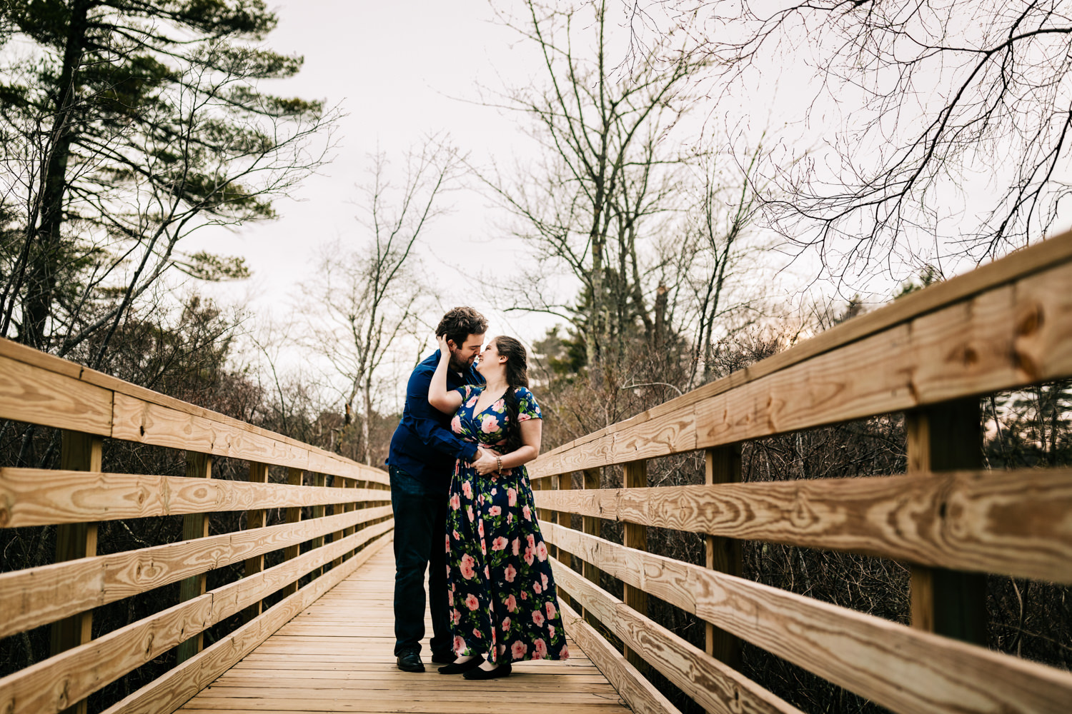 Couple on bridge over lake near Boston Massachusetts wearing blue floral dress