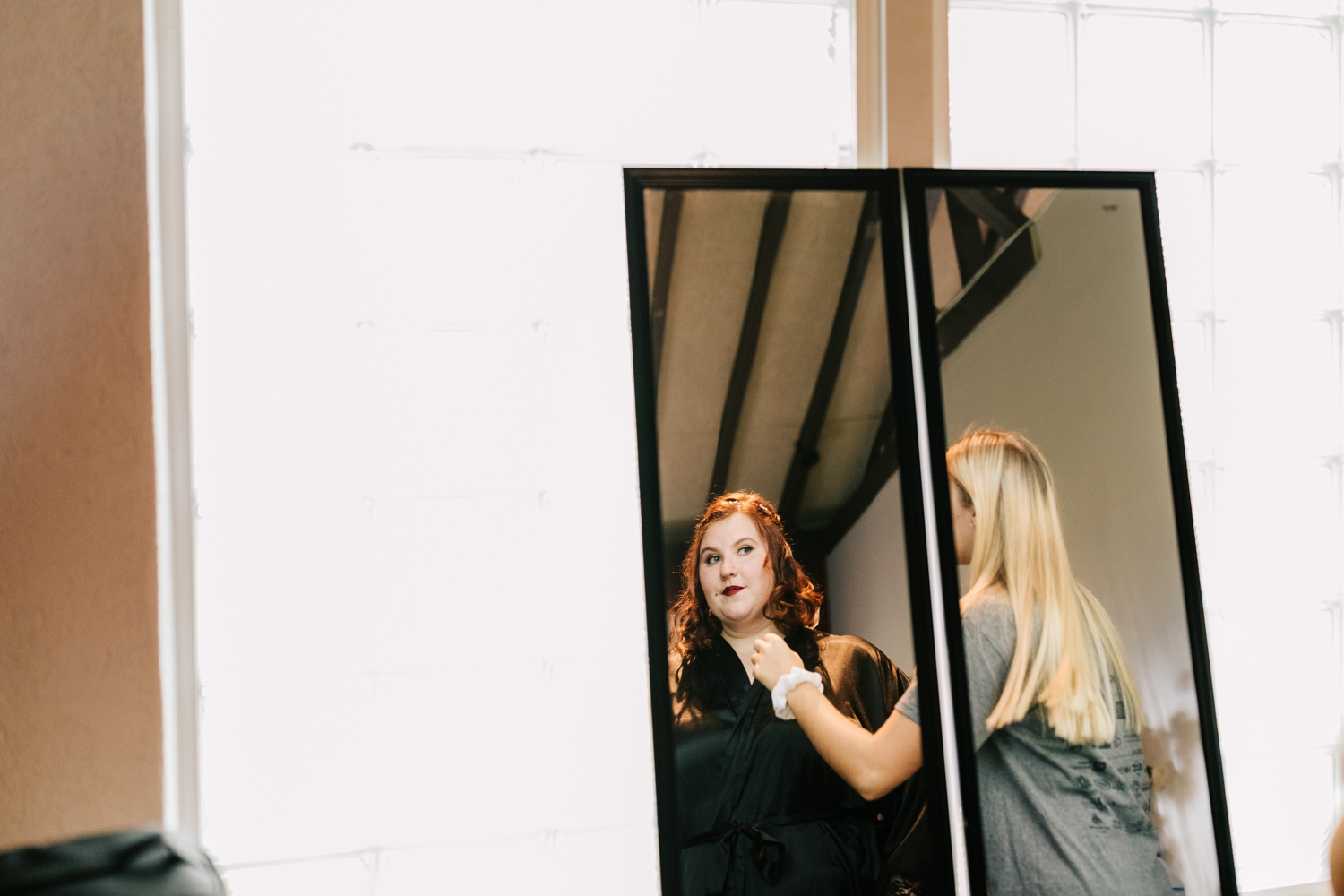 Redhead bride looking in mirror on wedding day wearing red lipstick